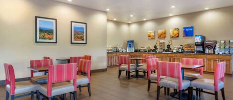 A hotel dining area with booths and tables, a kitchen in the background, and artwork on the walls.