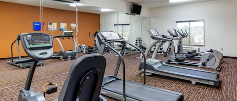 A gym with treadmills, elliptical machines, and a mirrored wall.