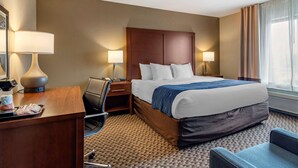 A hotel room with a large bed, two bedside lamps, a desk with a lamp, a chair, and a tray with items on it.