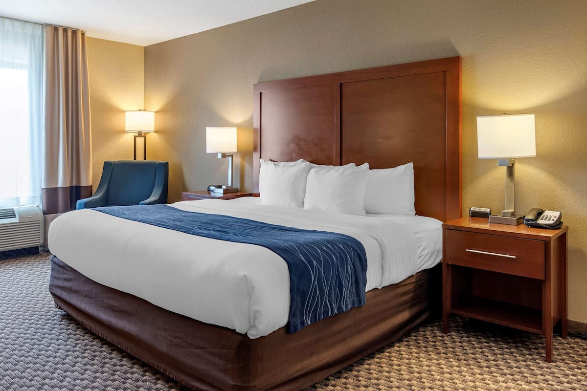 A hotel room with a large bed, two bedside tables, a chair, and a lamp.