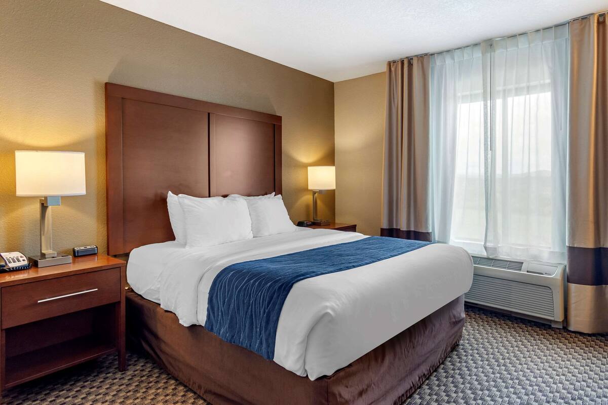 A hotel room with a large bed, two bedside tables with lamps, a telephone, and a window with curtains.
