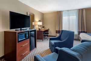 A hotel room with a flat-screen TV, a desk with a lamp, a microwave, and a seating area with two chairs.