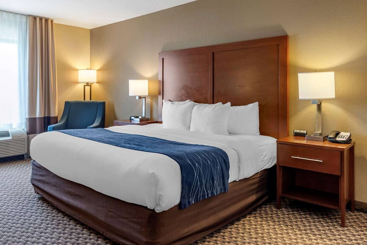 A hotel room with a large bed, two bedside tables with lamps, a chair, and a window with curtains.