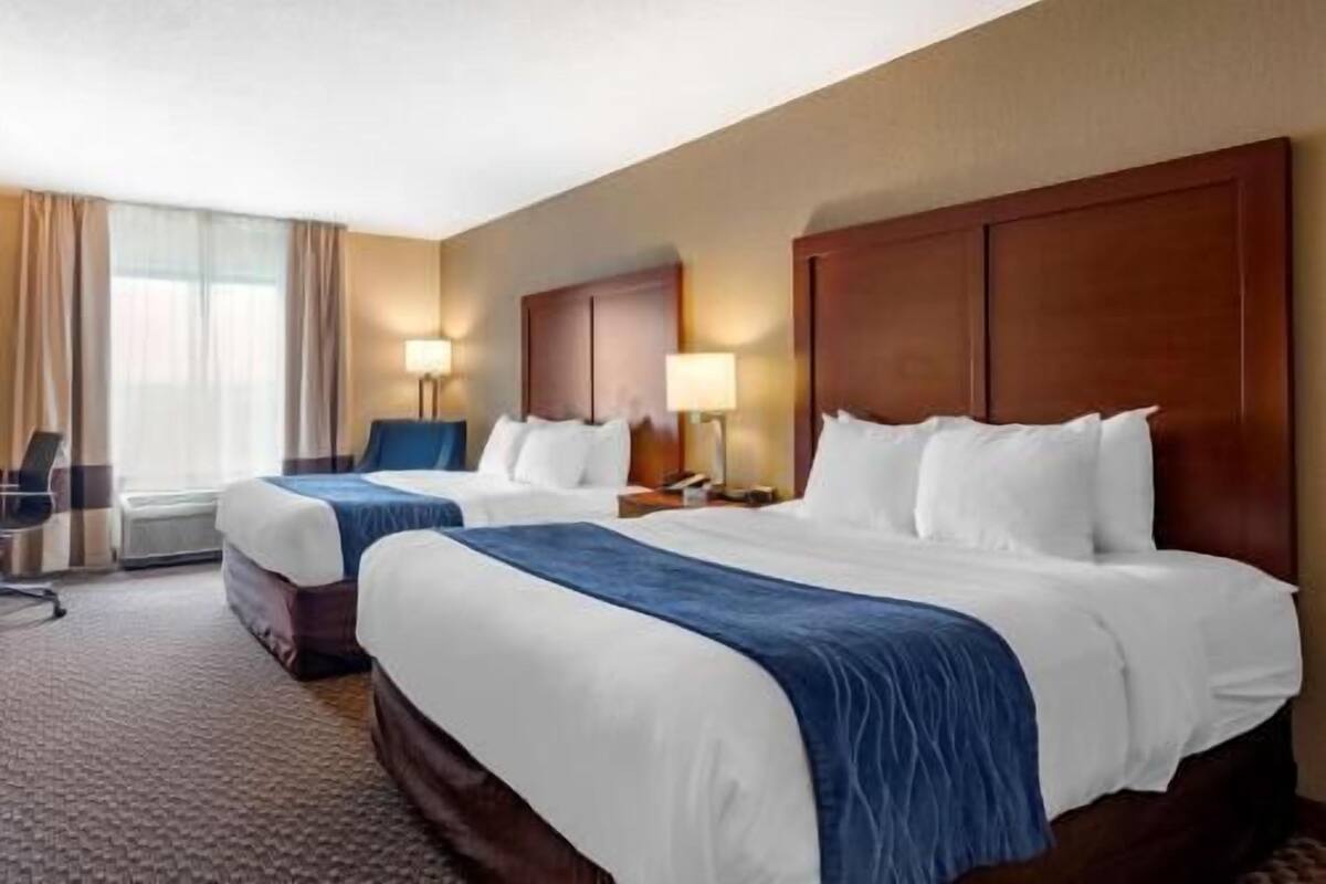 A hotel room with two beds, a desk, and a chair.