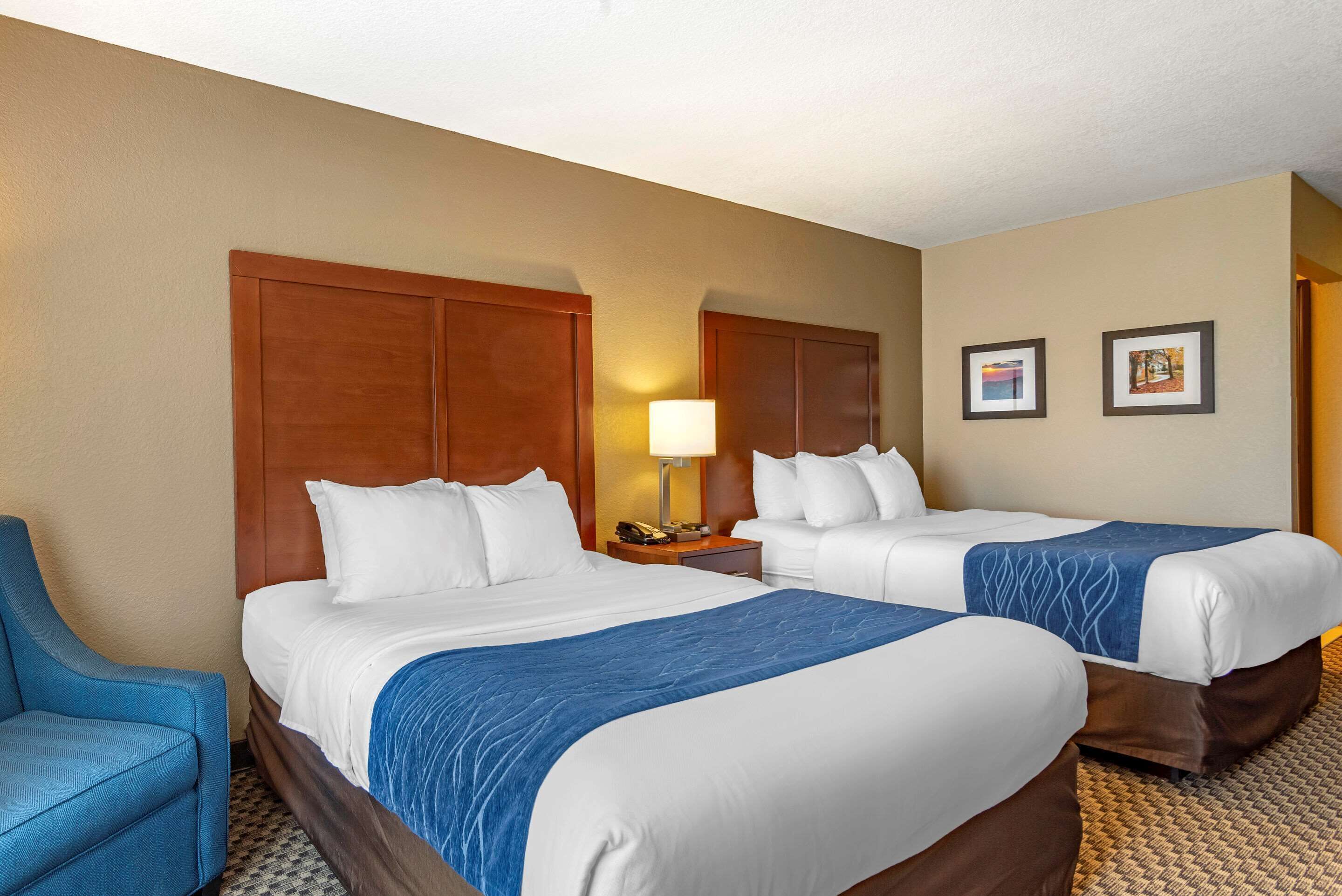 A hotel room with two beds, a desk with a lamp, and a chair.