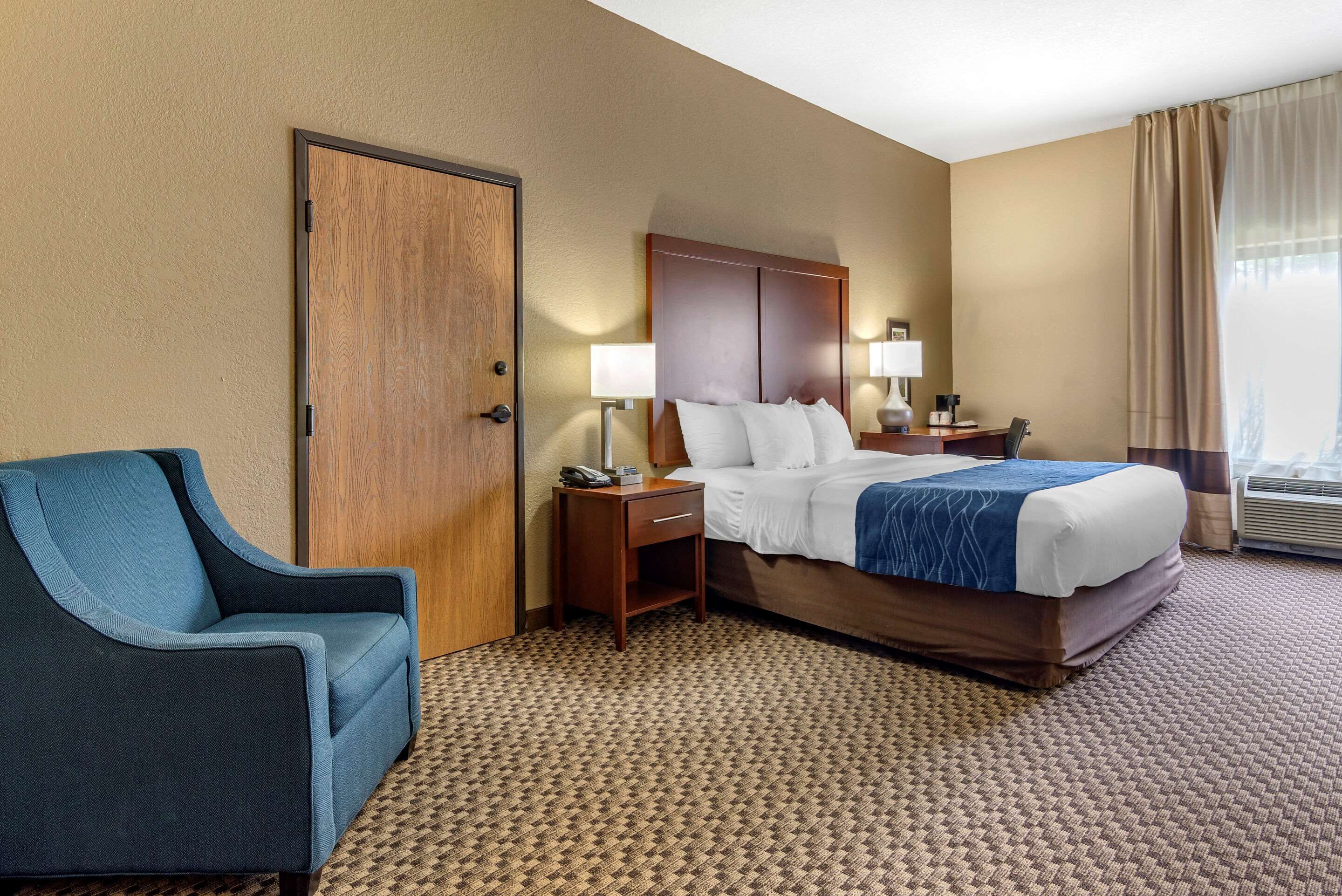 A hotel room with a bed, a desk, a chair, and a door.