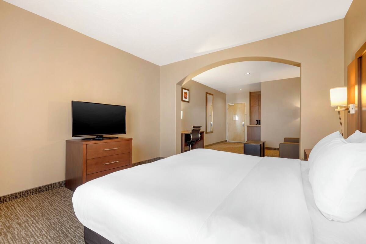 A hotel room with a large bed, a TV on a wooden cabinet, a desk with a chair, and a mirror on the wall.