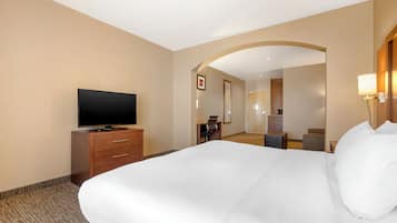 A hotel room with a large bed, a TV on a wooden cabinet, a desk with a chair, and a mirror on the wall.