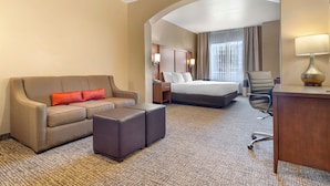 A hotel room with a sofa, ottoman, bed, desk, and lamp. - Comfort Inn at Convention Center (St. George)