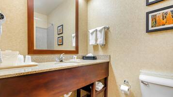 A bathroom with a wooden vanity, a sink, a mirror, a toilet, and two framed pictures on the wall.