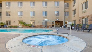 A hotel pool area with a hot tub, lounge chairs, and a building with multiple windows. - Comfort Inn at Convention Center (St. George)