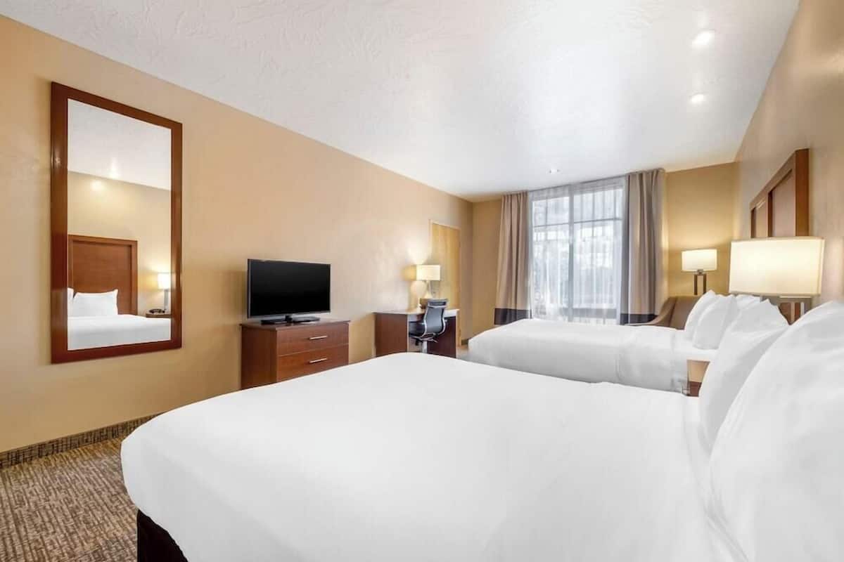 A hotel room with two beds, a television, a desk, and a window with curtains.
