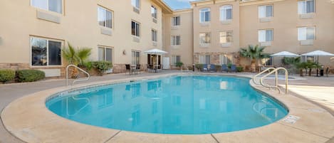 A hotel courtyard with a swimming pool, outdoor seating, and a building with multiple windows.