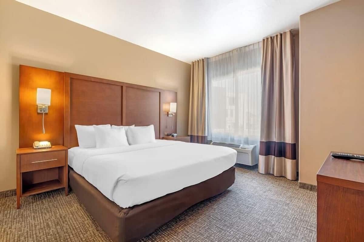 A hotel room with a large bed, a nightstand with a lamp, a desk with a remote control, and a window with curtains.