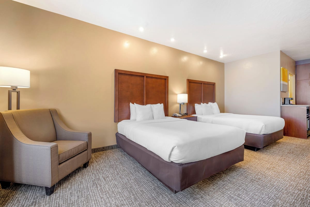 A hotel room with two beds, a sofa, a desk, and a lamp.
