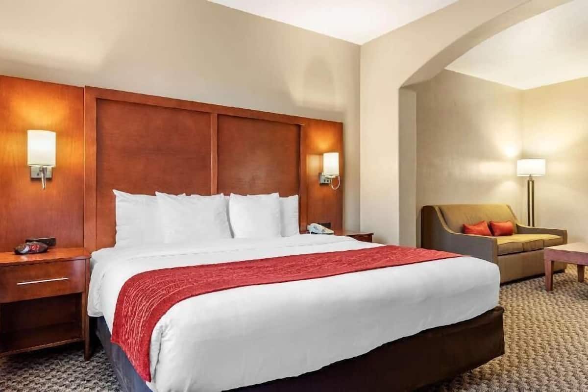A hotel room with a large bed, bedside tables, a chair, a lamp, and a wall-mounted light fixture.