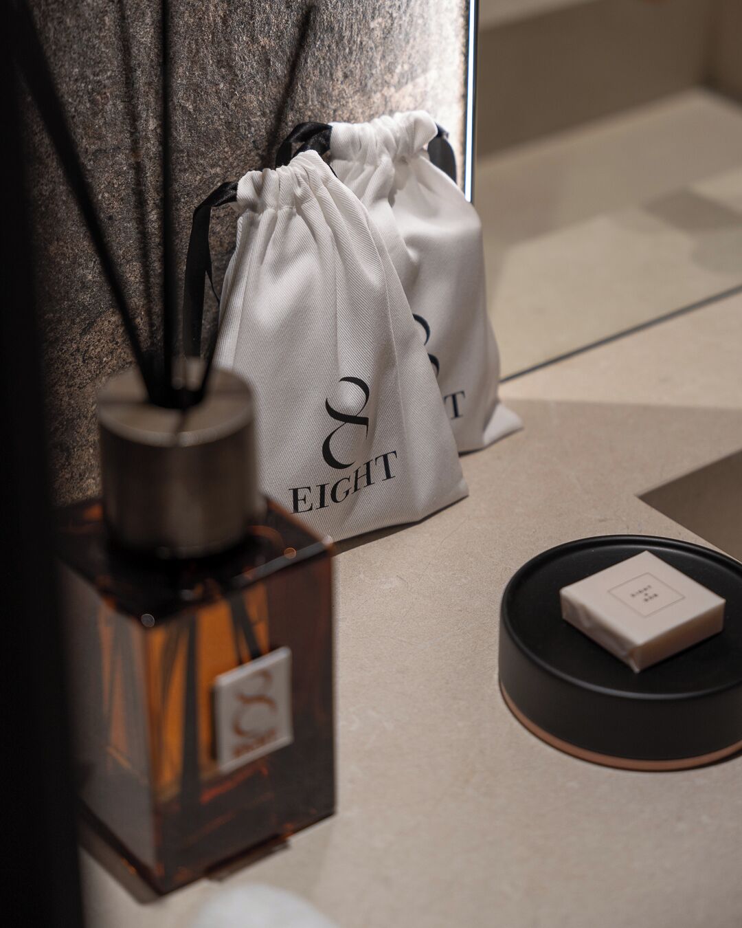 Una botella de perfume, una cajita y dos bolsas de cordón con el texto '& EIGHT'.