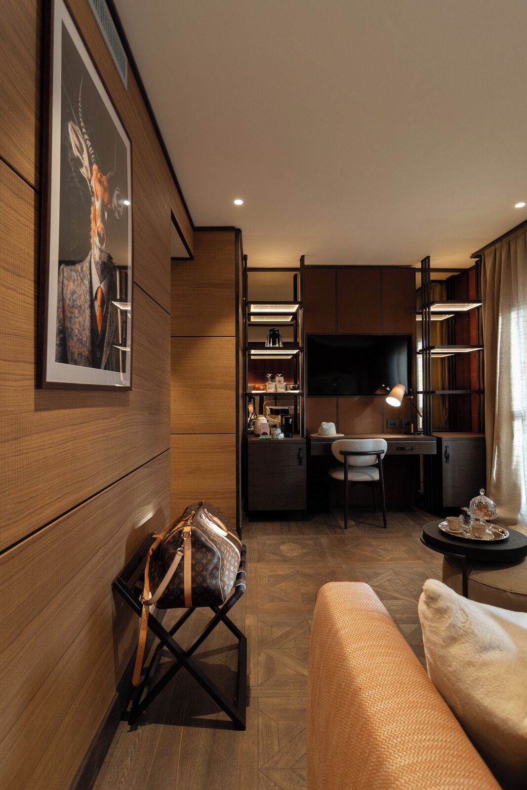 A compact hotel room with a bed, a desk, a chair, a TV, and a small kitchenette.