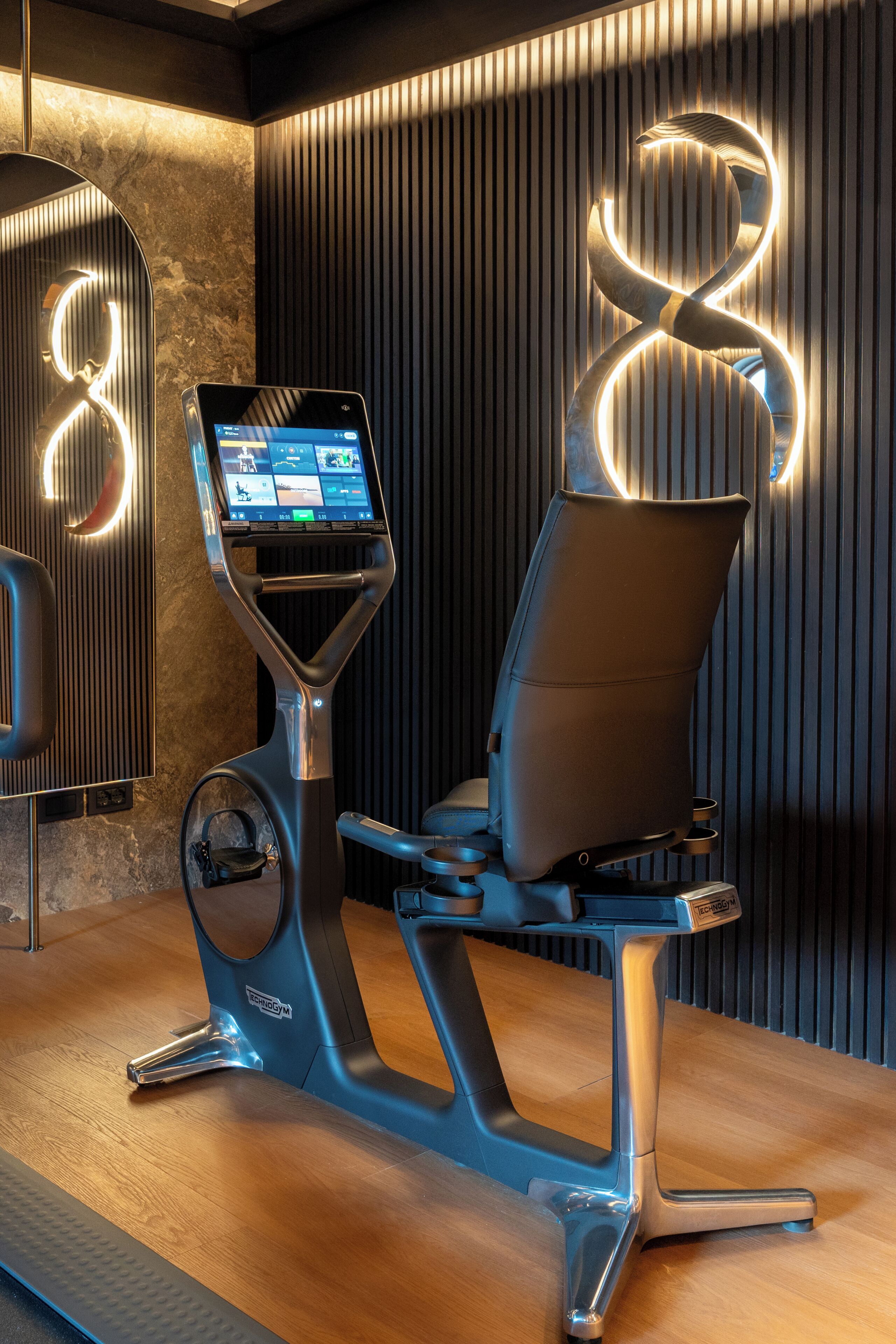 Uma bicicleta ergométrica com tela digital, um letreiro de madeira com o número 8 e um piso de madeira.