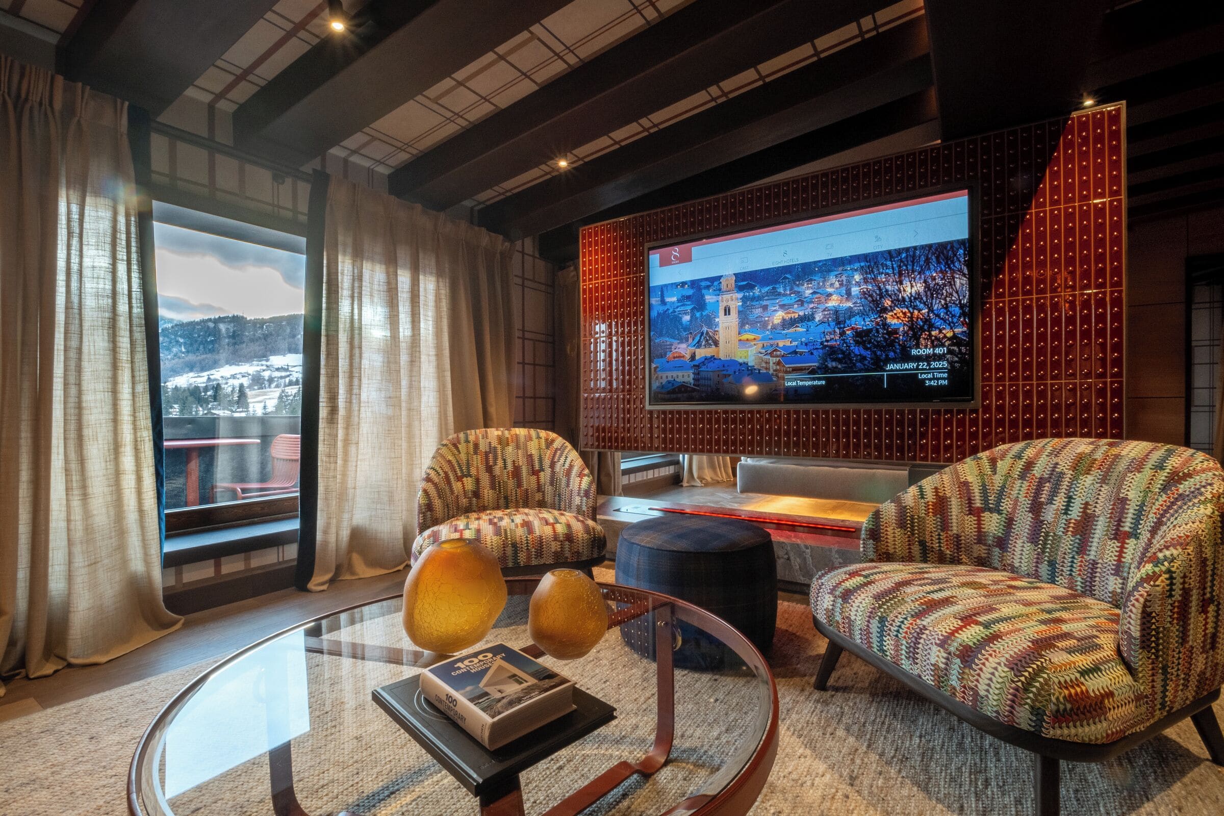 A modern living room with a large TV screen displaying a cityscape, comfortable seating, and a view of a snowy landscape through the window.
