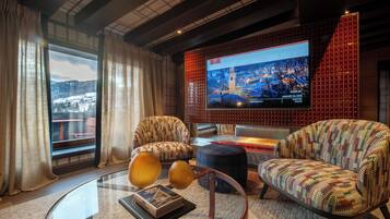 A modern living room with a large TV screen displaying a cityscape, comfortable seating, and a view of a snowy landscape through the window.