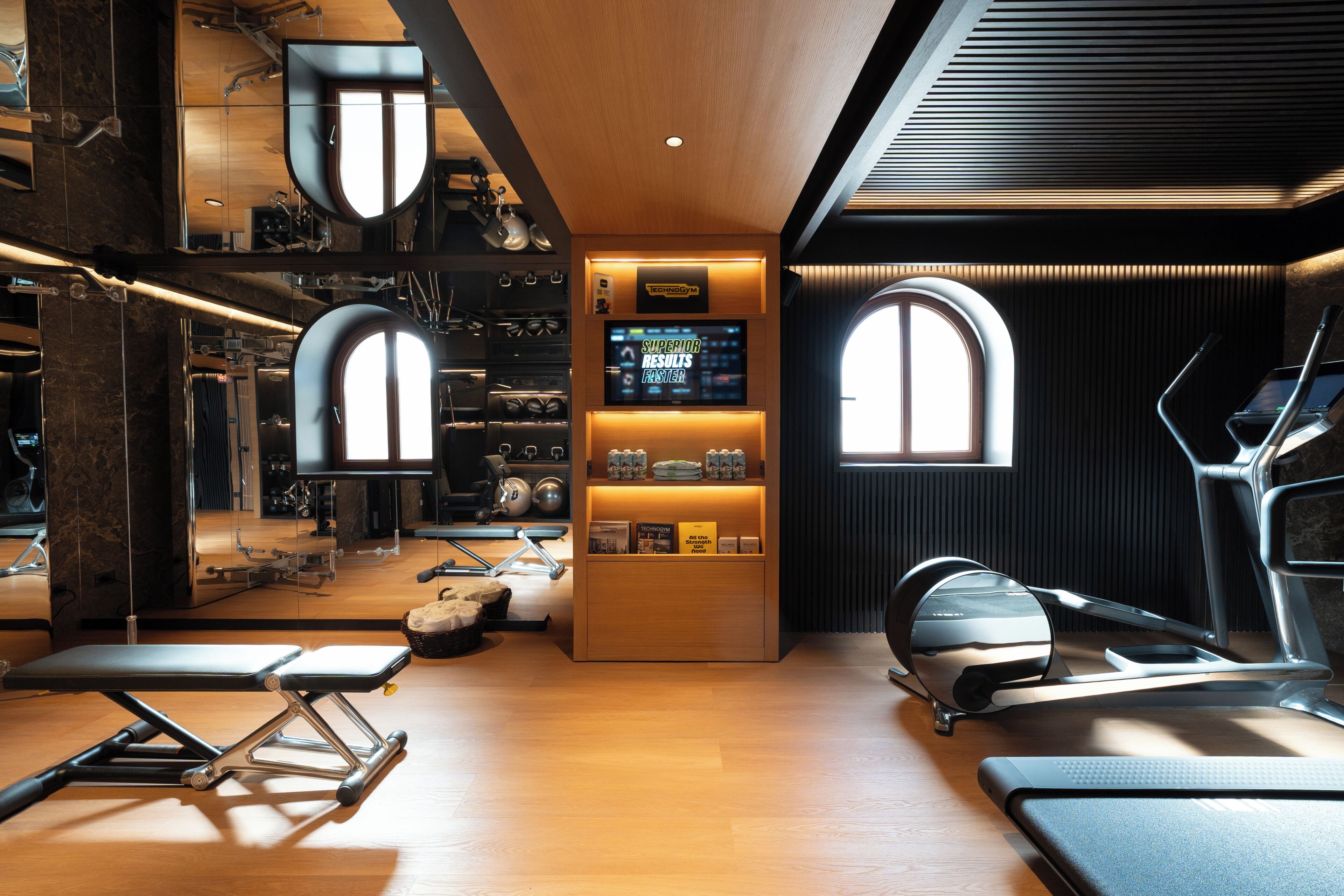Una palestra moderna con attrezzature da allenamento, una televisione che mostra contenuti di fitness e una reception in legno.
