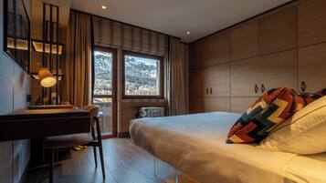 Ein modernes Hotelzimmer mit einem großen Bett, einem Schreibtisch mit Lampe und Blick auf Berge durch die Fenster.