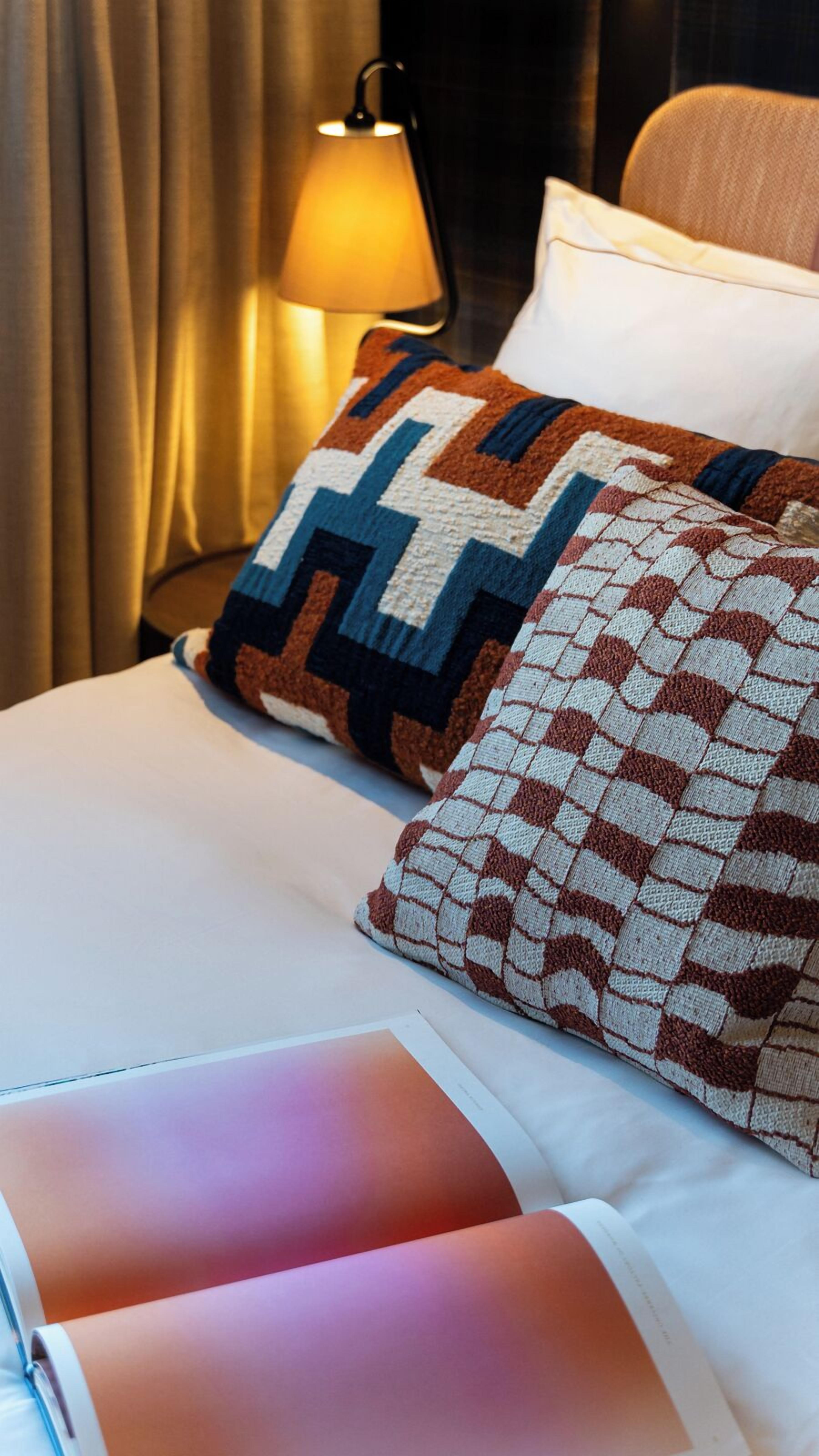 A neatly made bed with patterned pillows, a bedside lamp, and a curtain.
