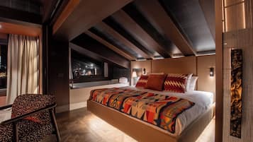 A modern bedroom with a large bed, a chair, and a view of the city at night.