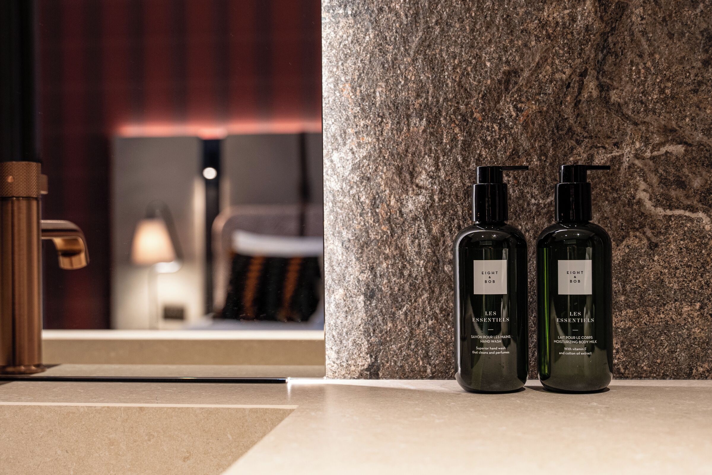 Un baño con una columna de mármol, dos botellas de loción y un grifo de cobre.