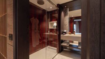 A modern bathroom with a glass shower enclosure, a vanity with a mirror, and a shelf with toiletries.