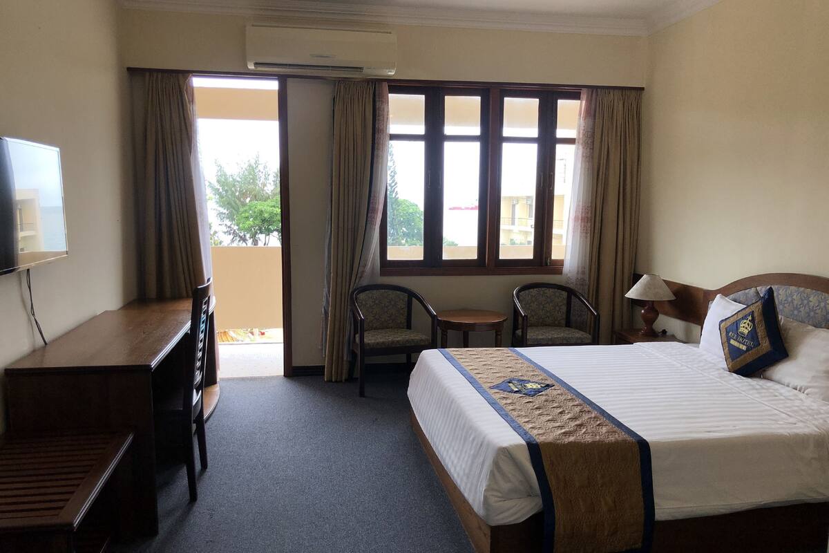 Habitación de hotel con cama, escritorio, dos sillas, televisor y ventana con cortinas.