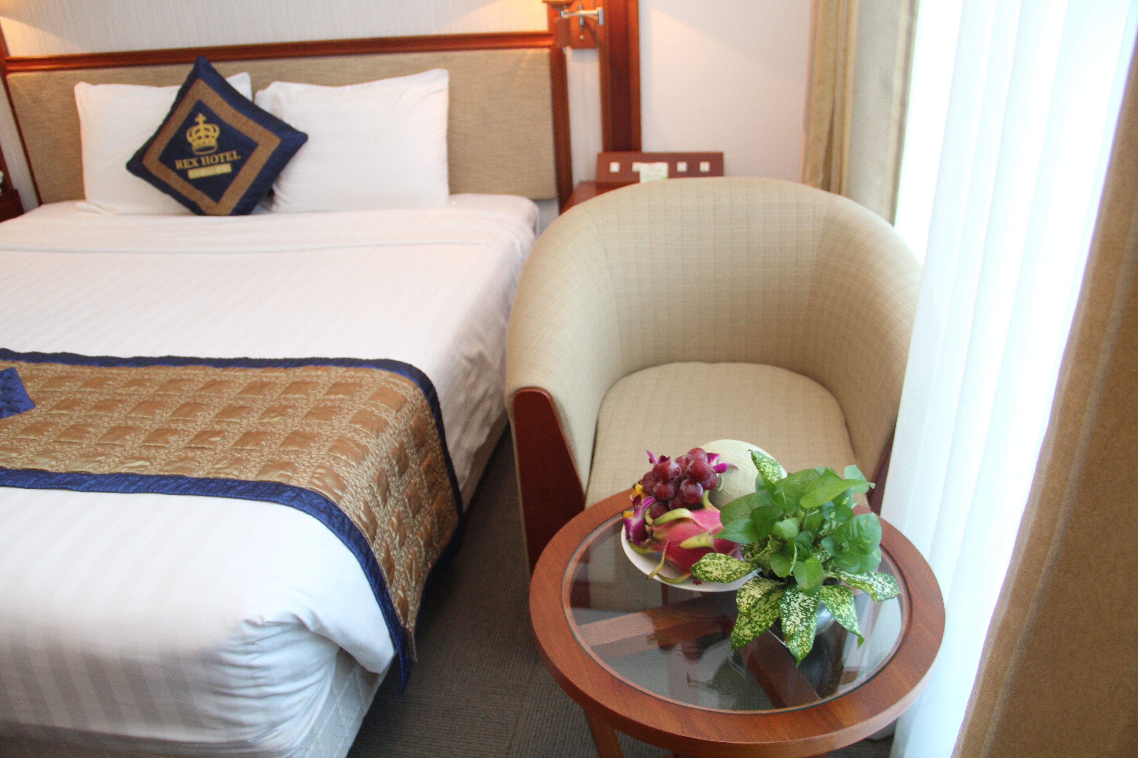 A hotel room with a bed, a chair, and a small table with a fruit bowl.