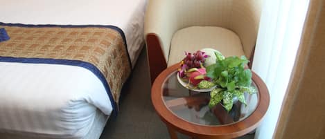 A hotel room with a bed, a chair, and a small table with a fruit bowl.