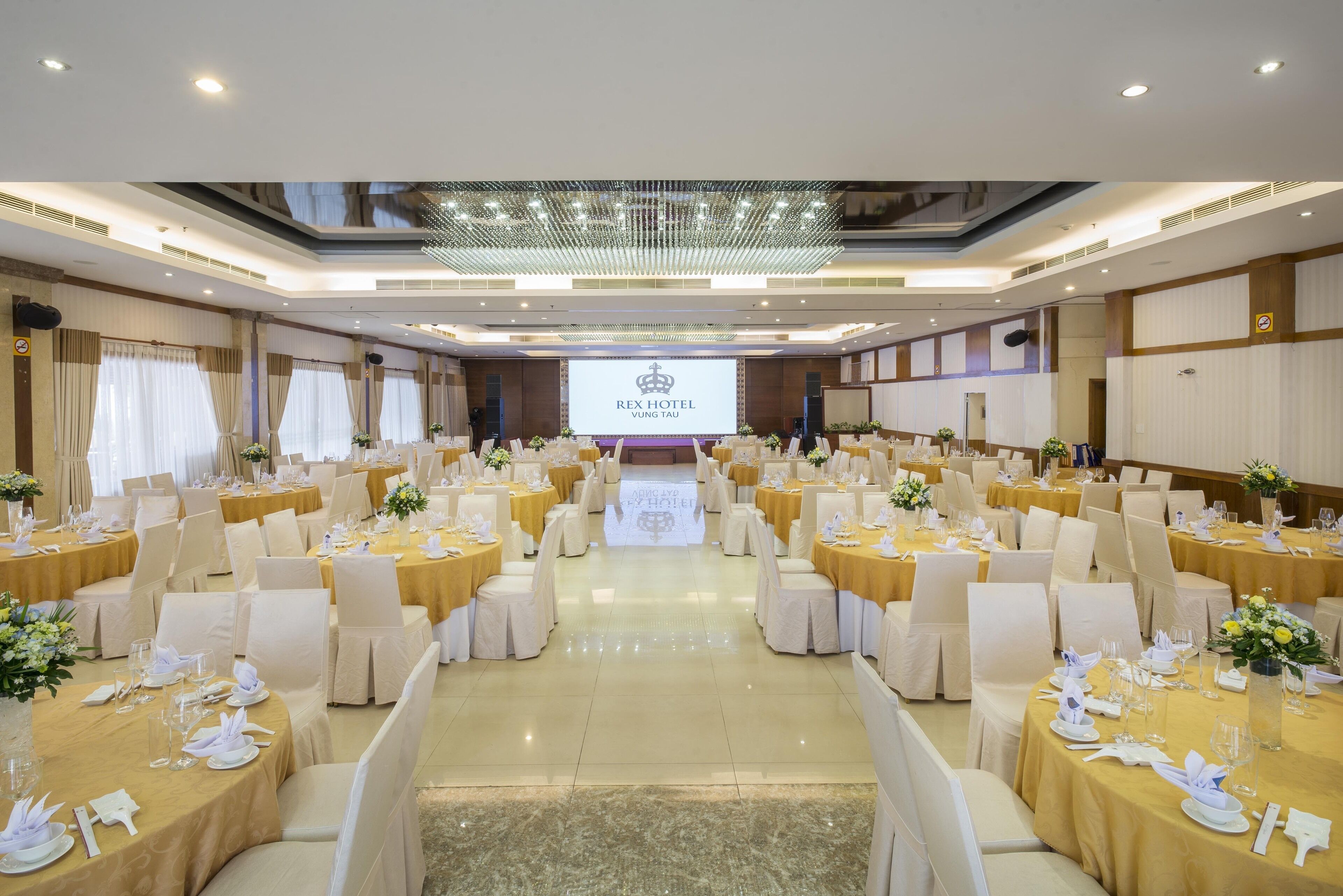 A banquet hall with round tables, white chairs, and yellow tablecloths.