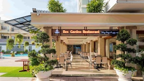 Restaurant Rex Garden mit Außenbereich, Topfpflanzen und einem Pool im Hintergrund.
