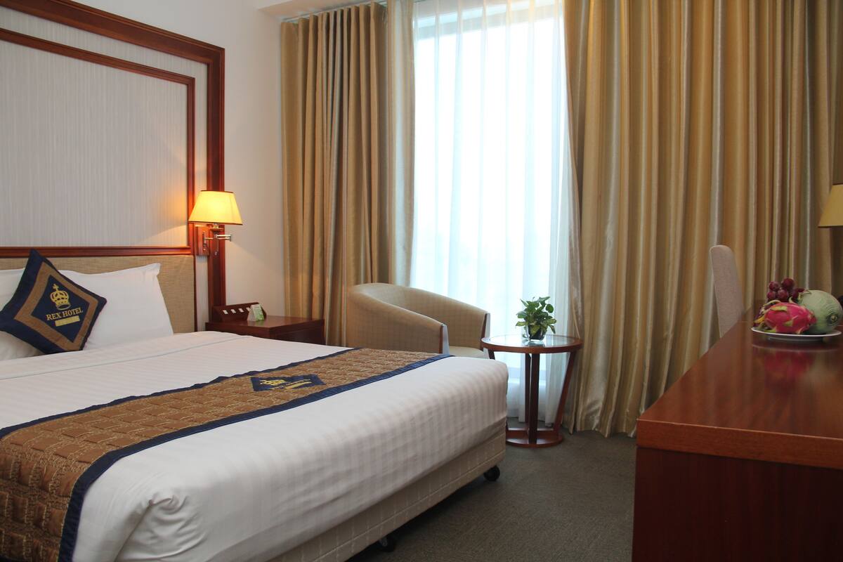 Una habitación de hotel con una cama grande, una silla, una mesita con una planta y un escritorio con fruta.
