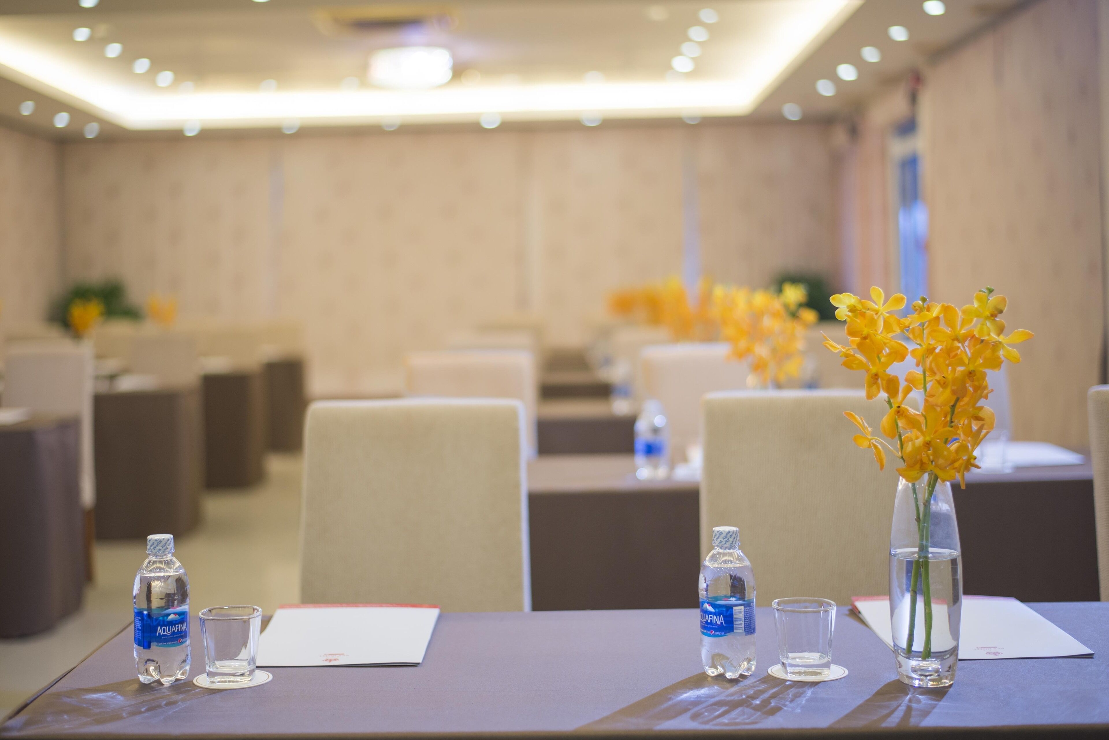A conference room with tables, chairs, water bottles, and vases with yellow flowers.