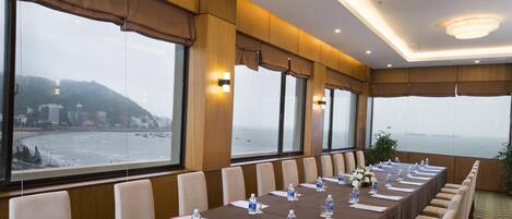 A conference room with a long table, chairs, water bottles, and a view of the sea.