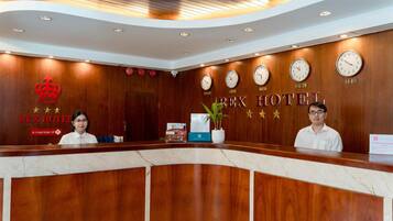 Een hotel receptiebalie met houten lambrisering, klokken die verschillende tijdzones tonen, en een bordje dat aangeeft dat het hotel deel uitmaakt van de REX hotelketen.