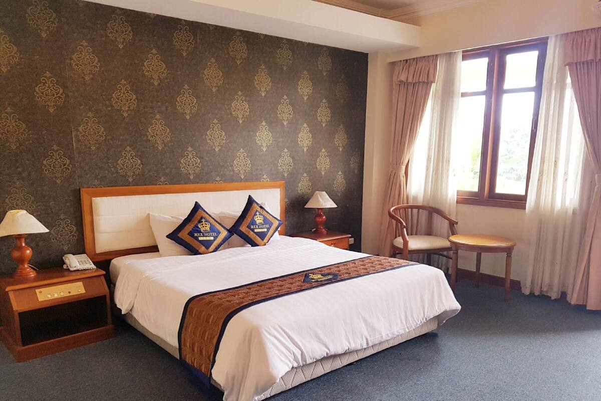 Habitación de hotel con una cama grande, dos mesitas de noche, una silla y una ventana con cortinas.