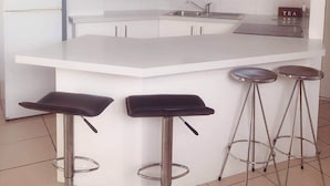 A modern kitchen with a white island, bar stools, and a microwave. - Windsurfer Resort (Biggera Waters)