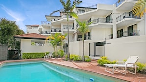 A swimming pool with lounge chairs, surrounded by a landscaped garden with palm trees and a multi-story building with balconies. - Windsurfer Resort (Biggera Waters)