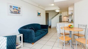 A living room with a blue sofa, a dining table with four chairs, and a kitchen in the background. - Windsurfer Resort (Biggera Waters)