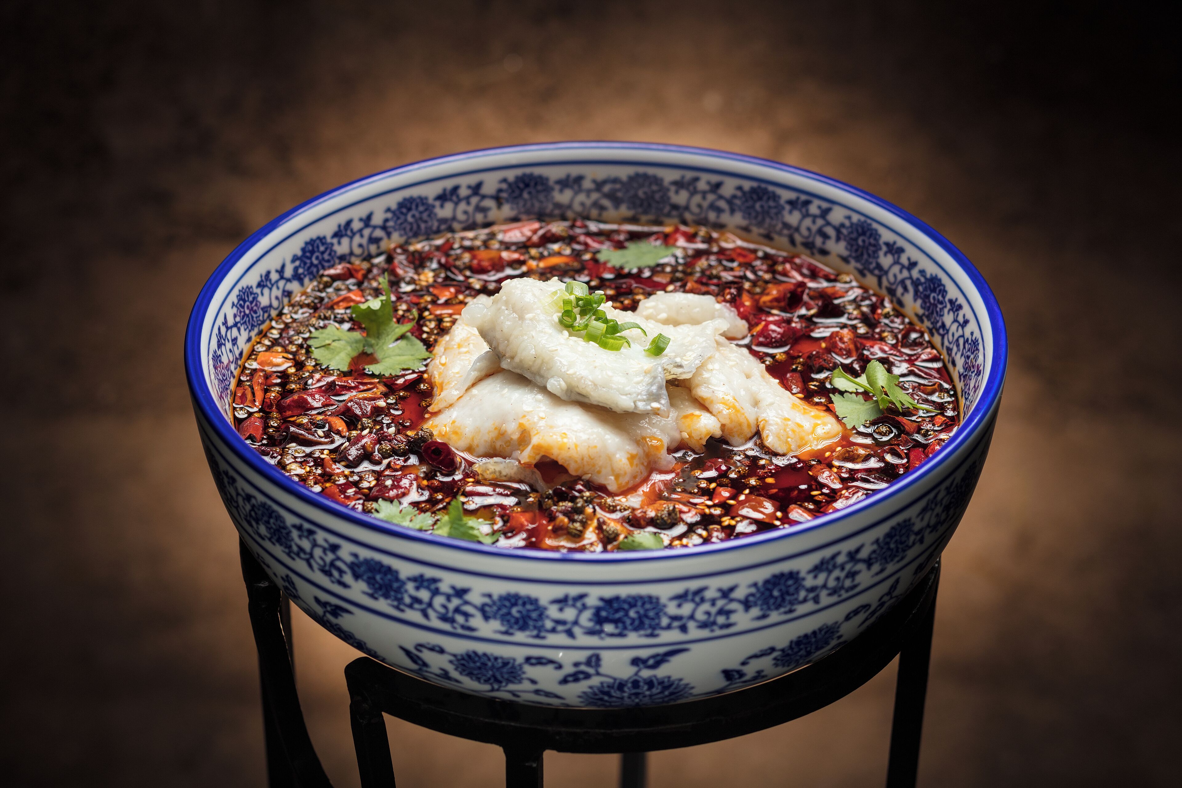 A bowl of food with a blue and white pattern, containing what appears to be dumplings and red chili flakes, garnished with green onions and cilantro.