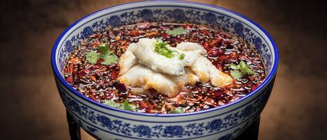 A bowl of food with a blue and white pattern, containing what appears to be dumplings and red chili flakes, garnished with green onions and cilantro.