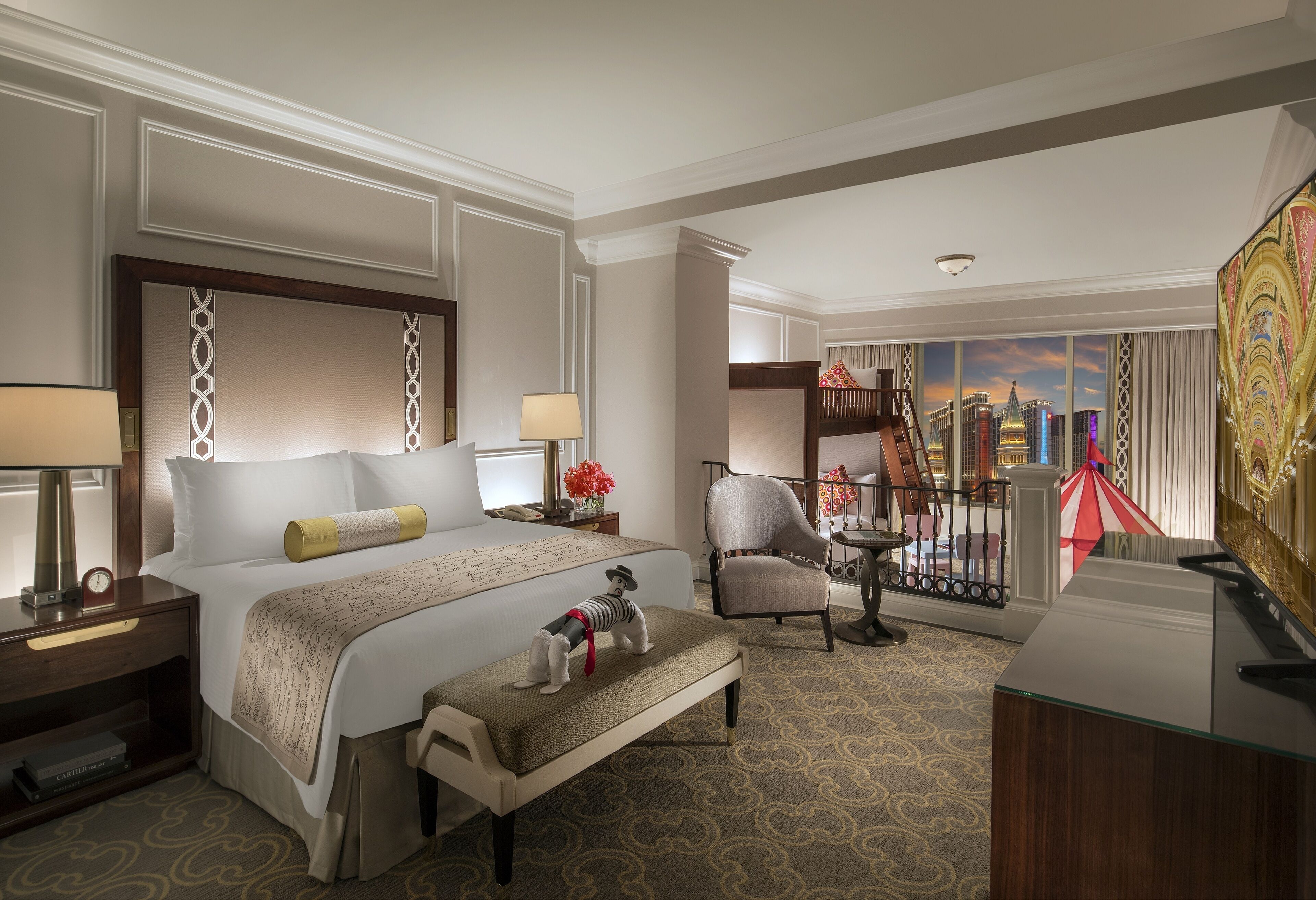 A hotel room with a large bed, a desk, a chair, and a balcony with a city view.
