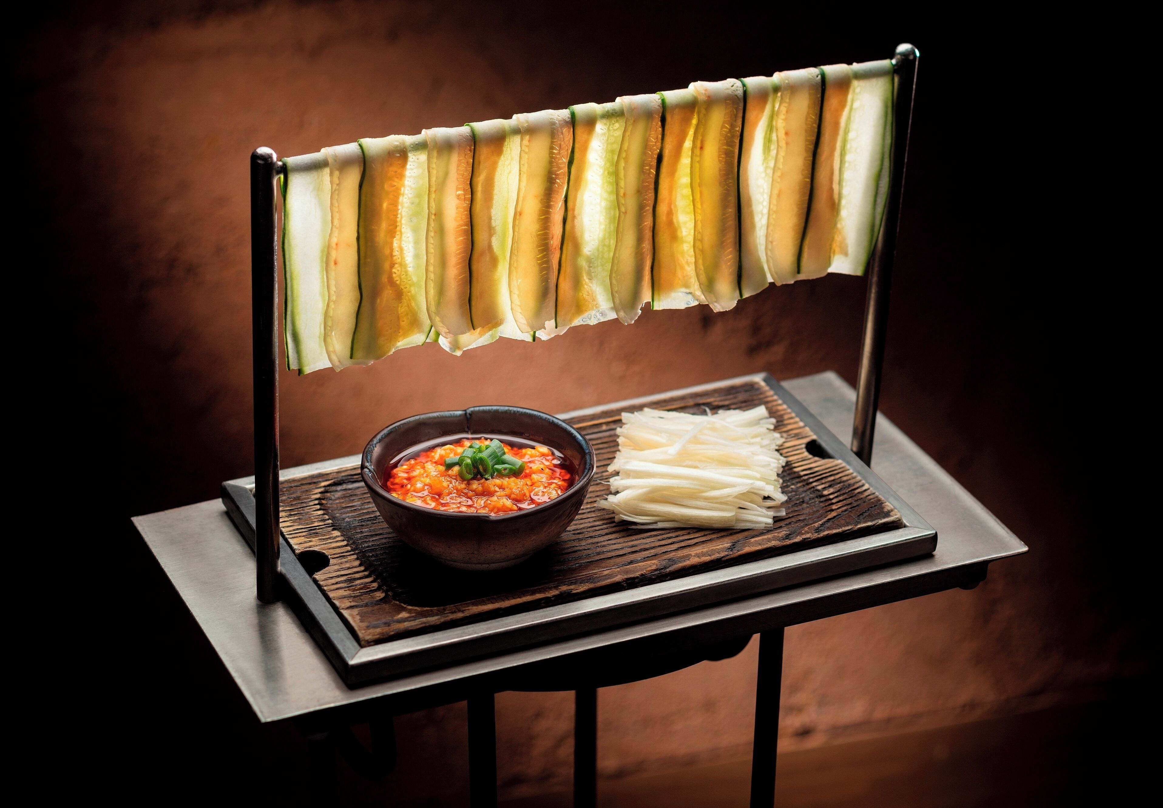 A table with a bowl of soup and sliced vegetables on a tray.