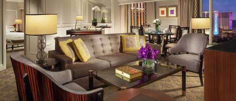 Habitación de hotel con sofá, sillones, una mesa de centro y zona de comedor.