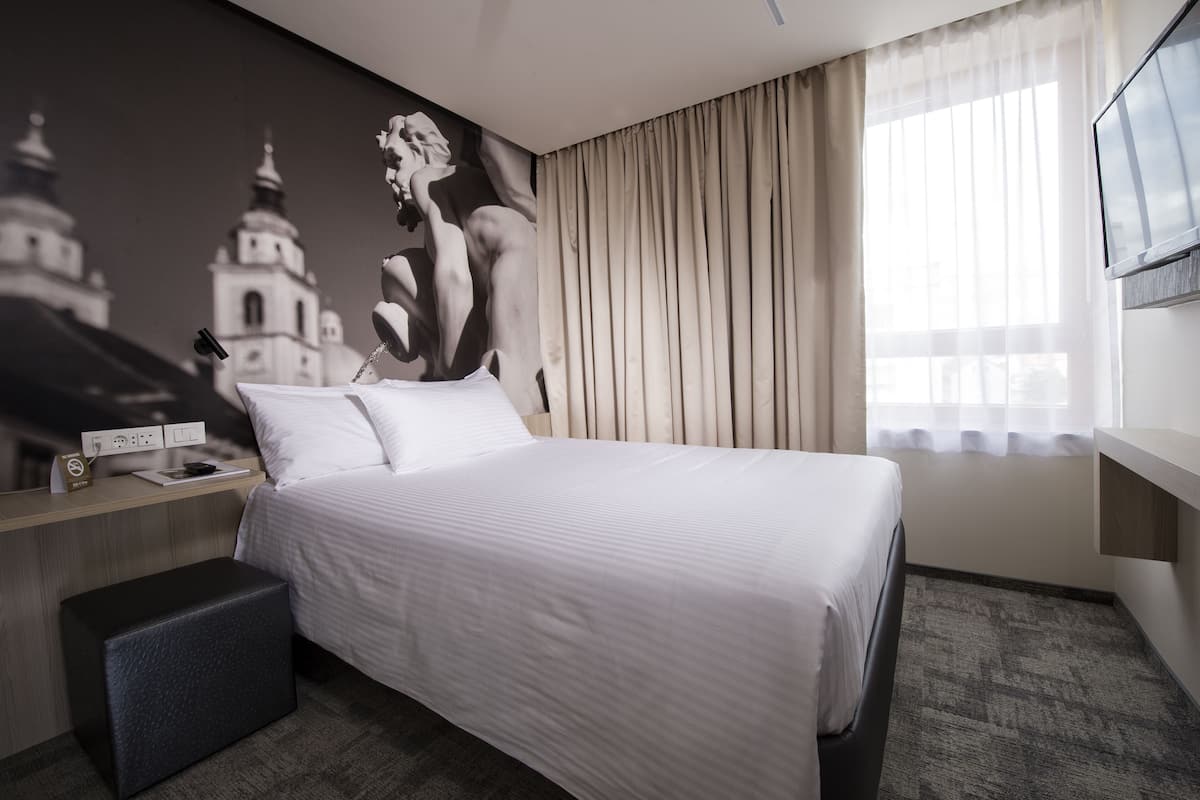 A hotel room with a large bed, a desk with a telephone, and a wall-mounted TV.